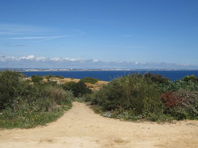 Sandy pathway leading to Cape St Vincent with blue sea and sky ahead, Algarve, Portugal