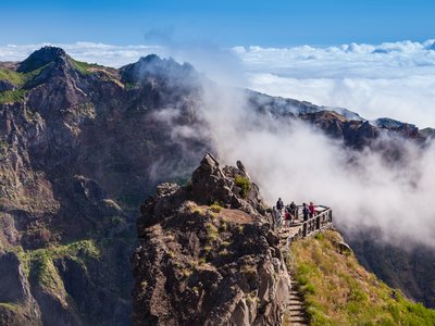 People trekking from Pico do Arieiro to Pico Ruivo standing at viewpoint surrounded by mountain landscape and clouds, Madeira island, Portugal