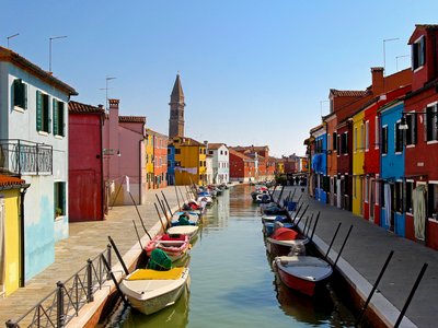 Boats docked on both sides of canal with colourful houses on sunny day, Burano Island in Venice, Italy