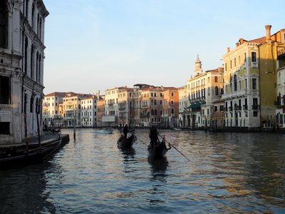 Sunlight casted onto top of houses in bending canal waterways with gondolas being steered in distance, Venice, Italy