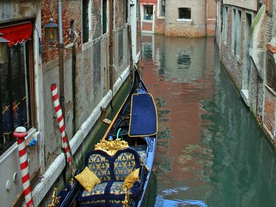  Highly decorated blue gondola in canal leaning against house, Venice, Italy