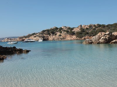 Transparent blue sea with coastal rocks forming safe place for boats to anchor in distance, Sardinia