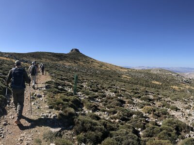 Three people walking in line on left towards hill in alpine tundra Sierra de las Nieves, Andalucia, Spain