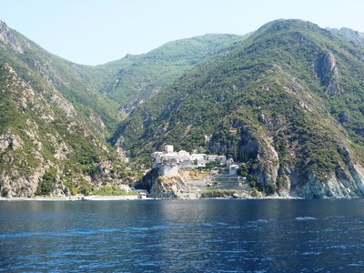 Building nestled in bottom of mountainside near water edge, viewed from across water, Greece
