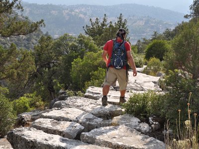 Person hiking St Paul Trail following large stone pathway with pine trees growing close by, along Yenikoy to Adada and Sagrak, Turkey